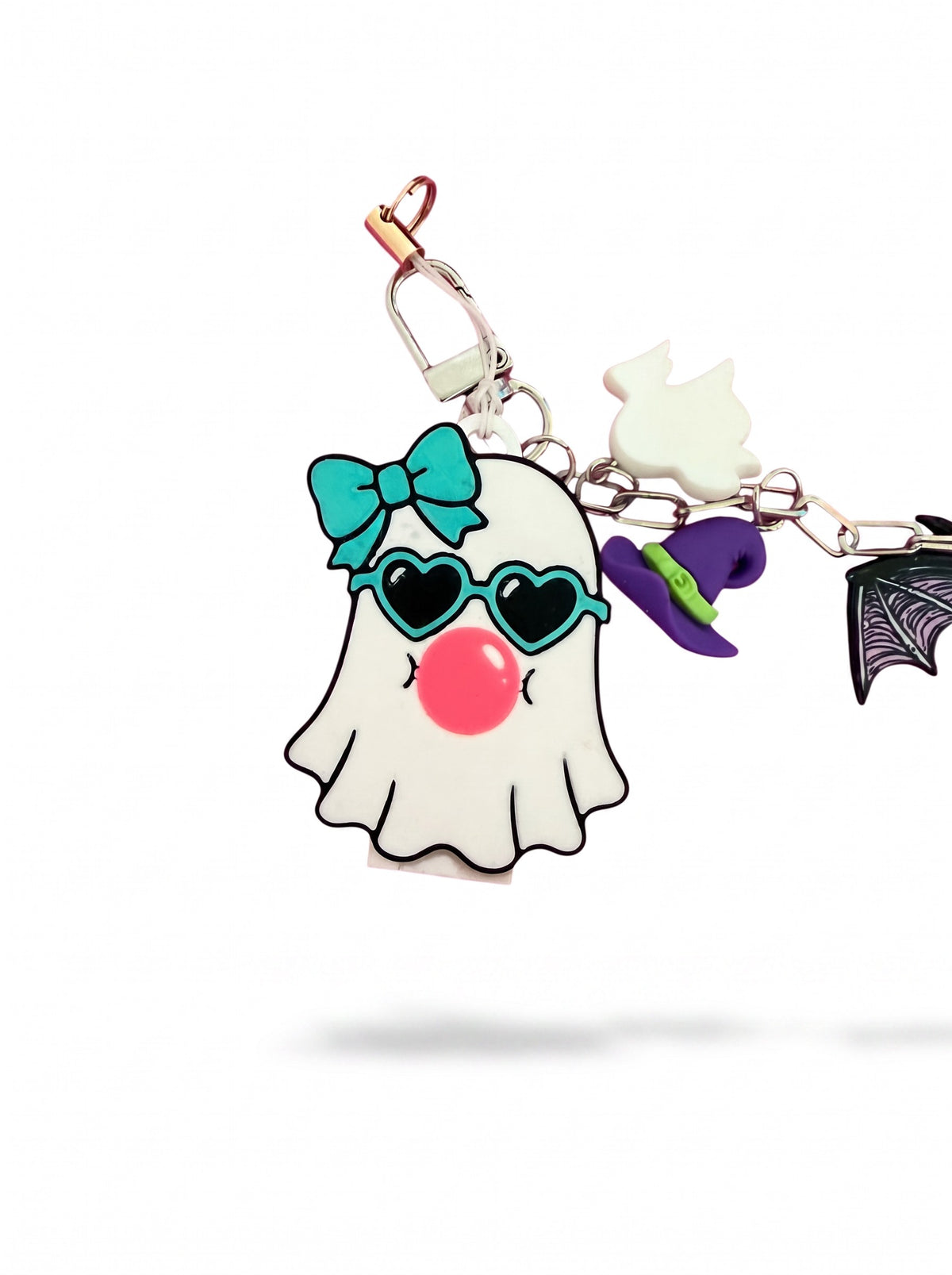 A Halloween-themed keychain or bag charm featuring a white ghost character with a turquoise bow, heart-shaped sunglasses, and a pink nose, attached to a metal clasp with small dangling charms including a white cat silhouette, a purple witch hat, and a black bat wing on a white background.