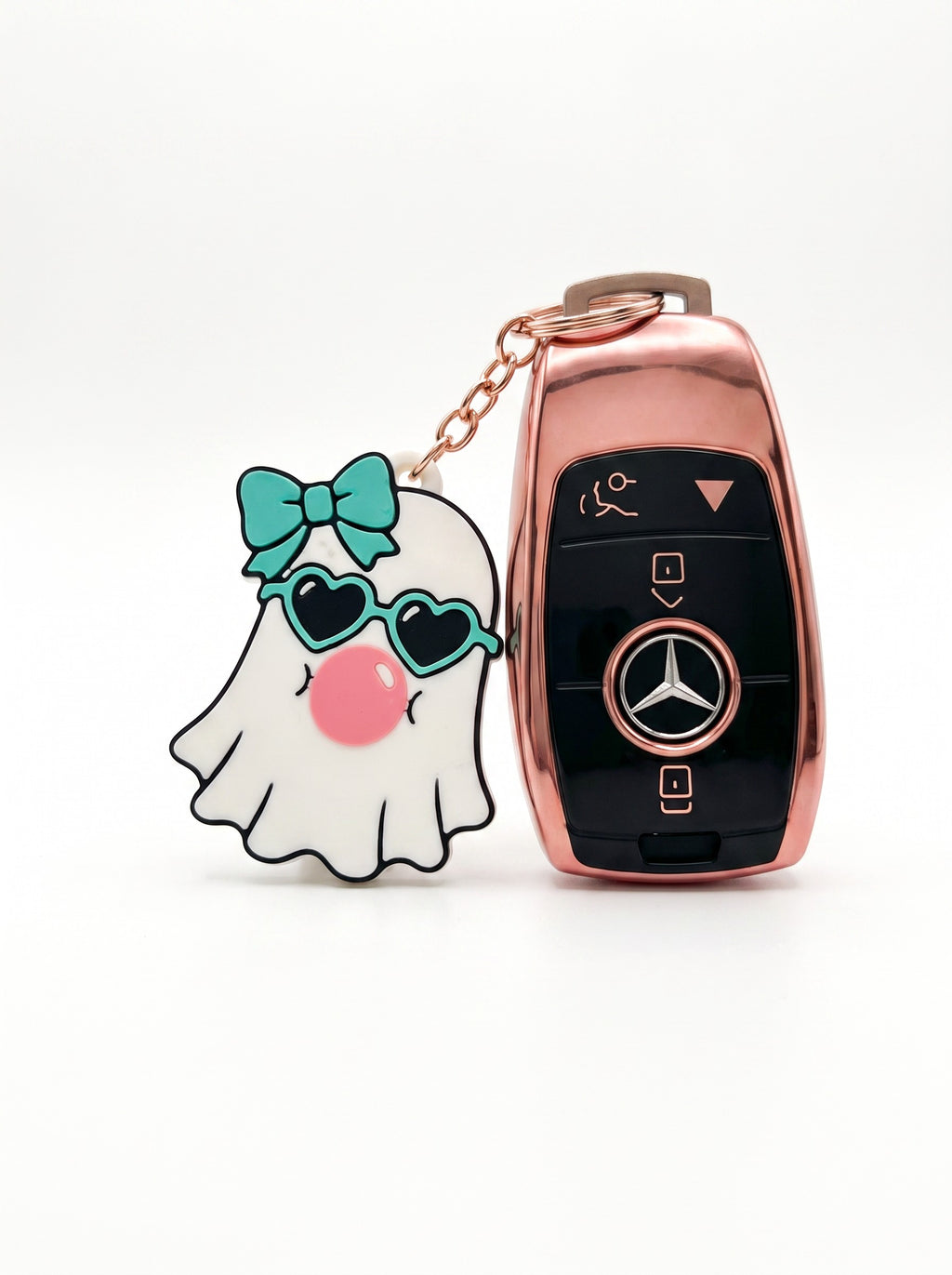 A rose gold Mercedes-Benz key fob case with a matching keychain featuring a cute white ghost charm wearing a teal bow and heart-shaped sunglasses.