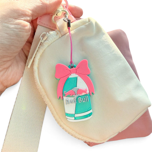 Pink bow energy-drink can PopOff keychain attached to a cream crossbody bag