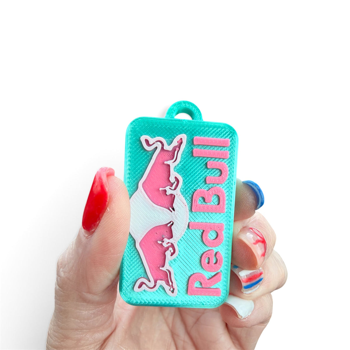 Pocket Magic Redbull PopOff keychain in teal with pink logo held in a hand with vibrant nail art