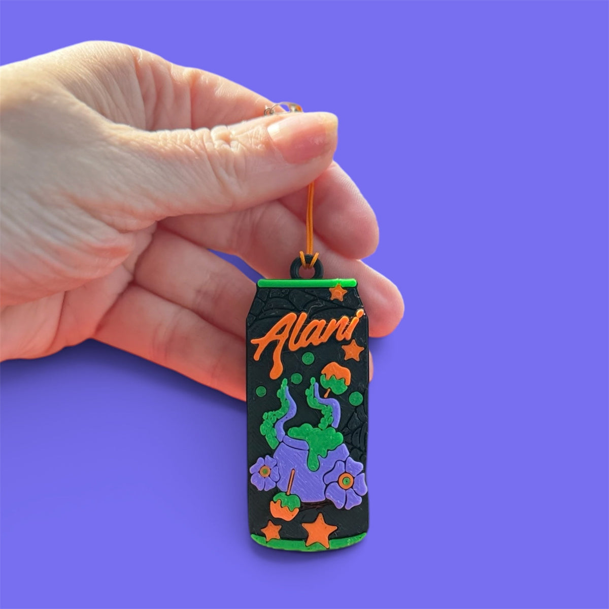 Black, purple, green, and orange Witches’ Brew PopOff can-tab opener held against a purple background